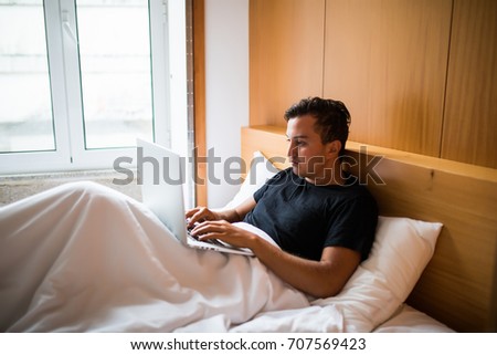 Young man lying in the bed working on a laptop