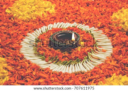 Flower rangoli for Diwali or Pongal made using marigold or zendu flowers and red rose petals over white background with Clay Oil Lamp in the middle, selective focus