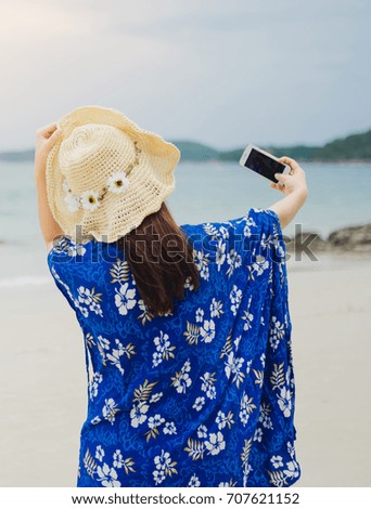 A young woman wearing a hat is taking a picture by selfie at a beautiful beach.