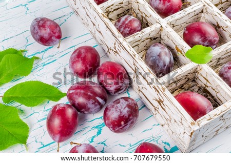 Plums in a wooden box with cells with green foliage on the table