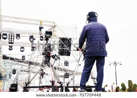Cameraman using black professional digital video camera. Outdoor setup and working