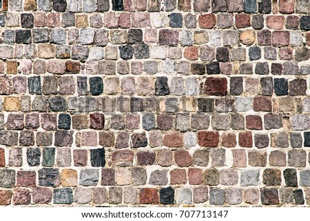 Medieval stone wall texture background. Old stone blocks are primarily of reddish and blue color under natural sunny daylight. Some restoration work to preserve original wall structure is seen.