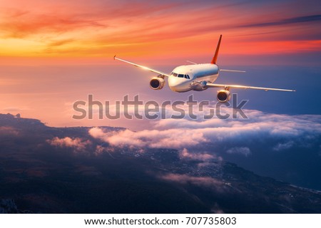Passenger airplane. Landscape with big white airplane is flying in the sky over the clouds and sea at colorful sunset. Passenger aircraft is landing at dusk. Business trip. Commercial plane. Travel Royalty-Free Stock Photo #707735803