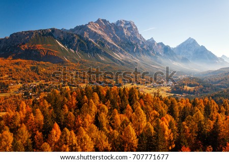 Amazing aerial view of the Dolomite Alps at sunny autumn day with yellow larches below and valley covered by fog and high mountain peaks behind. Cortina d'Ampezzo, Veneto, Italy.  Royalty-Free Stock Photo #707771677