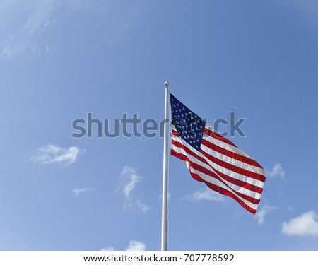 American flag flapping in the wind with blue sky and small cloud background