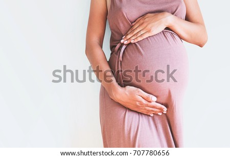 Pregnant woman in dress holds hands on belly on a white background. Pregnancy, maternity, preparation and expectation concept. Close-up, copy space, indoors. Beautiful tender mood photo of pregnancy. Royalty-Free Stock Photo #707780656