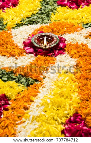 flower rangoli for Diwali or pongal or onam made using marigold or zendu flowers and red rose petals over white background with diwali diya in the middle, selective focus
