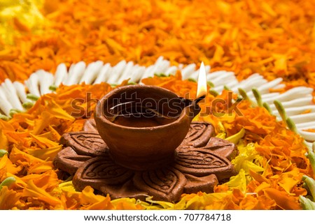 flower rangoli for Diwali or pongal made using marigold or zendu flowers and red rose petals over white background with Clay Oil Lamp in the middle, selective focus
