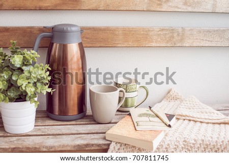 a brown thermos on the wooden bench with two cups and book Royalty-Free Stock Photo #707811745