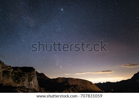 Night on the Alps under starry sky and the majestic rocky cliffs on the Italian Alps, with Orion constellation at the horizon.