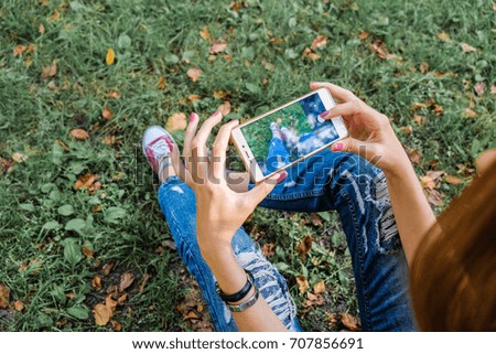Hipster girl using her smartphone with empty screen to copy paste. Young successful woman sitting on social networks and read messages. Girl taking pictures on smartphone.