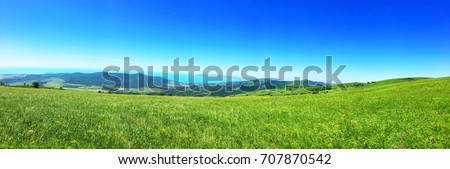 Panorama summer flower meadow in the mountains, tourism. Beautiful sea view landscape. Fresh green rural meadows on a sunny day with blue sky. Scenery view ocean