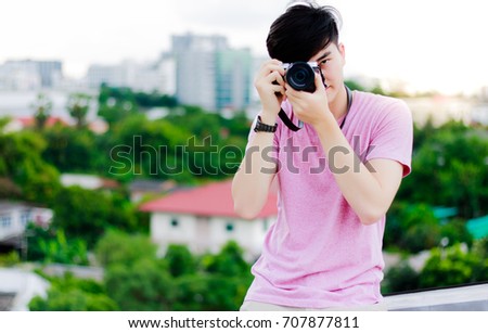 Portrait student handsome young boy: A handsome student man practices taking photo by his favorite camera on the top of building with beautiful cityscape and natural background.