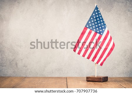 Retro USA flag on wooden table front old concrete wall background. Vintage instagram style filtered photo
