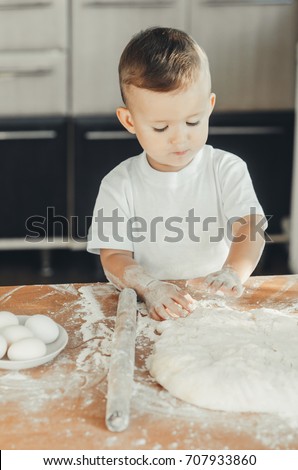 The little Boy in the kitchen himself in a white t-shirt hard kneads the dough
