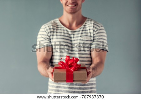 Cropped image of handsome young man holding a gift box and smiling, on gray background