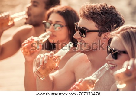 Happy friends are drinking soda water and smiling while resting at the sea