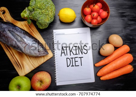Atkins Diet on chalkboard, health conceptual. Healthy fresh food fish, lemon, tomatoes, apple, carrot and broccoli. Royalty-Free Stock Photo #707974774