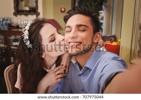 Young beautiful enamored couple sitting at a table in a cafe and making selfie