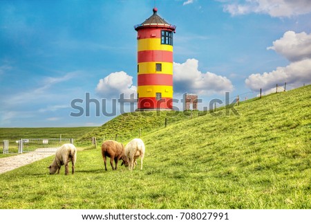 Sheep in front of the Pilsum lighthouse on the North Sea coast of Germany. Royalty-Free Stock Photo #708027991