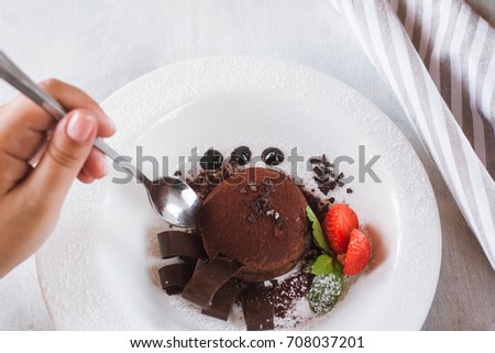 Tasting of delicious chocolate dessert in restaurant. Fondant on white plate with decoration from strawberry and mint for real gourmet