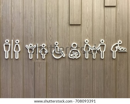 Public restroom signs for men, women, children, handicaps, nursery, family, diaper changing station available in public area. White 2d signage on a wooden wall background