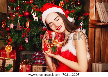 Young happy woman in red santa hat sitting near new year tree with present. Christmas concept.