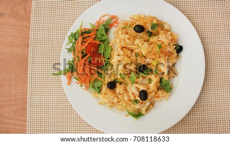 Traditional portuguese food Bacalhau on white plate at restaurant wooden table background. Codfish dish made with dried and salted cod, eggs, potato chips, olives. Served with small side green salad. 