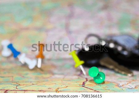 Travel destination points on a map indicated with colorful thumbtacks and shallow depth of field with space for copy. The keys to the car in the blur in the background. Selective focus.