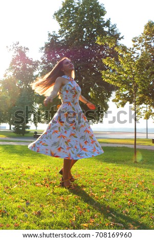 A beautiful young girl with long hair turns in the sun. The hair and dress of a woman are fluttering in the wind. Female happiness and a smile on the face of a beauty