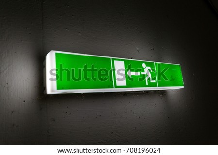Green shining escape exit sign on white concrete wall