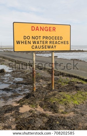 Sign warning of the danger and not to proceed when that water reaches the causeway at Lindisfarne, Northumberland, UK