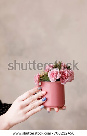 Beautiful pink roses in crimson cup holding in hands on beige wall. Festive background of love, early spring gift and blossom concept, free space above