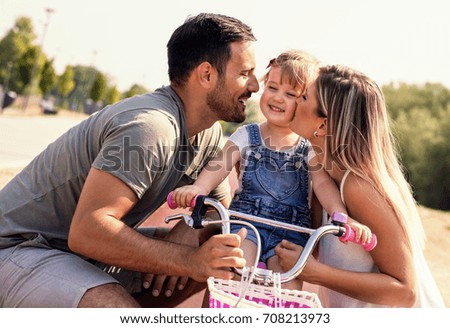Parents teaching daughter to ride a bicycle on beautiful sunny day
