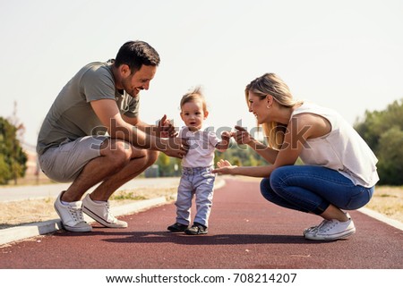 Young parents holding their little son making first steps  on beautiful sunny day

