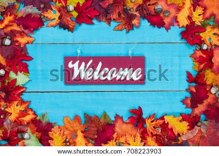 Welcome sign with colorful fall leaves border hanging on antique rustic teal blue wood door; autumn, Thanksgiving, Halloween, seasonal nature background with painted wooden copy space
