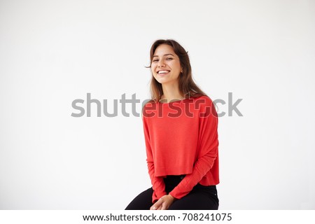 People, youth, joy, fun, leisure and happiness concept. Picture of carefree happy young Hispanic woman in casual red top relaxing in studio, sitting on chair, looking and grinning broadly at camera.