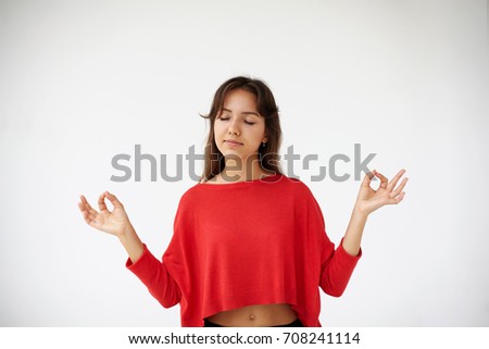 Isolated portrait of beautiful young mixed race woman practicing yoga and meditation in white studio, holding hands in symbolic gesture and keeping eyes closed, her body relaxed and mind calm.