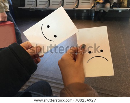 Smile and sad face on paper in man and woman hand