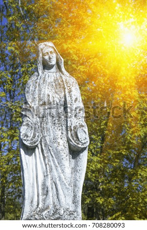 Virgin Mary statue in sun rays. Vintage sculpture of sad woman in grief (Religion, faith, suffering, love concept)