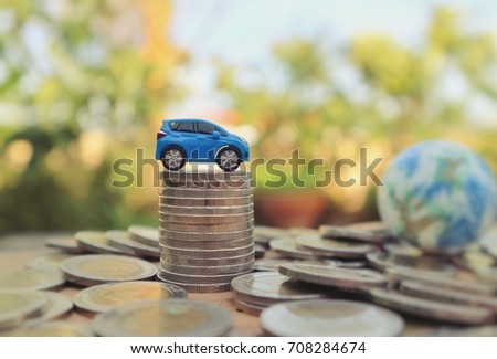 Toy car on pile of rolls coins and blur miniature world globe and pile of money in natural bright light bokek background,saving for goal concept