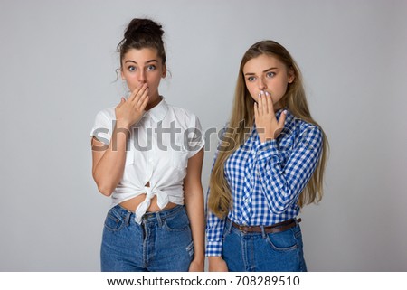 Two young sisters covering the mouth with their hands isolated on gray background.