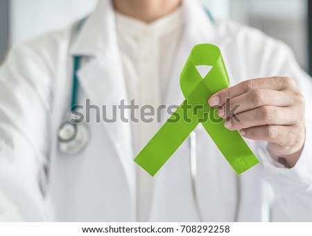 Lime green ribbon in doctor's hand for Lymphoma cancer and mental health awareness, raising support and help patient living with illness  Royalty-Free Stock Photo #708292258