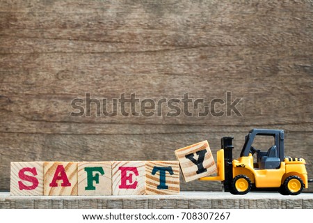 Toy plastic forklift hold block Y to compose and fulfill wording safety on wood background Royalty-Free Stock Photo #708307267