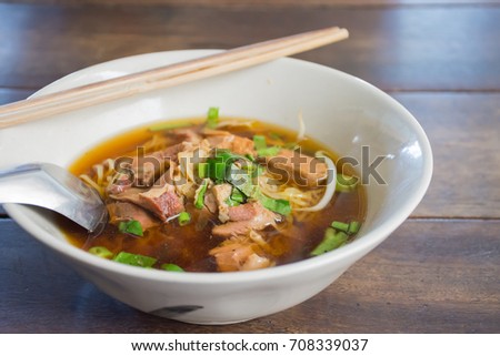Bowl of delicious stewed beef noodle soup in Thai style cuisine with chopsticks and spoon on wooden table