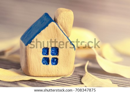 Miniature yellow toy house with a blue roof with bright yellow autumn leaves on a wooden surface. Toned. Selective focus. Autumn concept