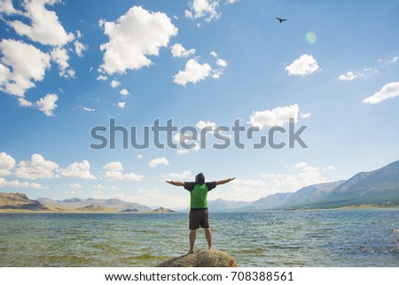 Man feeling freedom on beach during sunrise, birds flying around. rear back view of Man on the beach. hands up. male against lake with blue water and mountain