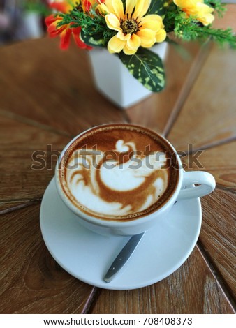 Queen of swan Lake picture in white ceramic cup of coffee latte art style on wooden table with vivid yellow flower background.
