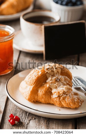 Continental breakfast with croissant, butter, jam, coffee and fruits. Closeup view, selective focus. Empty black chalkboard copy space for text