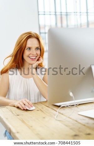 Excited young woman reading on the internet looking wide eyed at the computer screen with a pleased smile as she works indoors in an office
